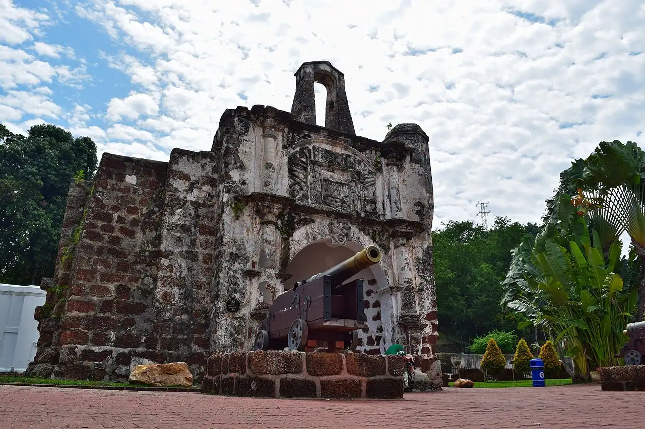 A Famosa fort gatehouse, an ancient stone structure with a cannon on a brick base, under a cloudy sky in Malacca, Malaysia