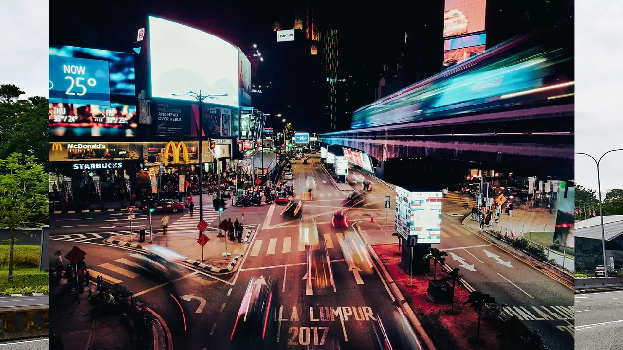 Long exposure photo of a bustling Bukit Bintang street at night with car light trails, a blur of a monorail, and bright billboards