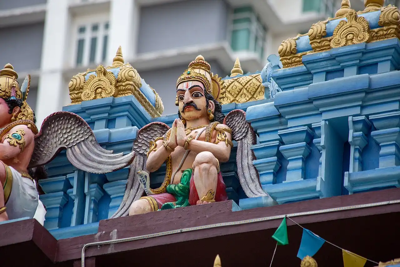 Detailed winged statue on a Hindu temple in Little India Brickfields, featuring blue and gold architectural elements.