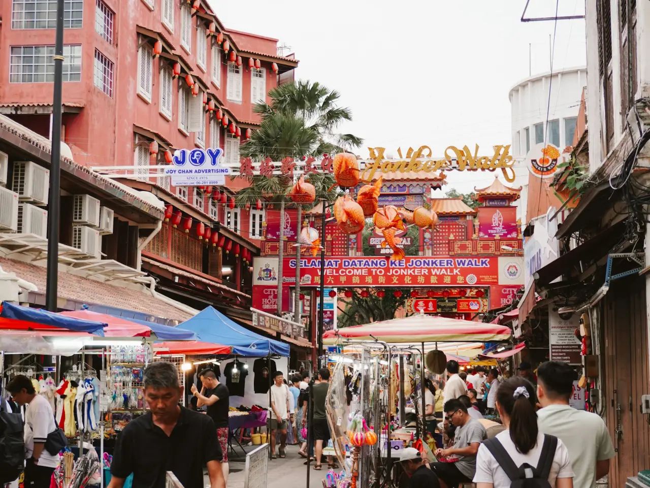 A vibrant market scene on Jonker Street Melaka, bustling with shoppers, colorful stalls, and traditional red buildings with lanterns