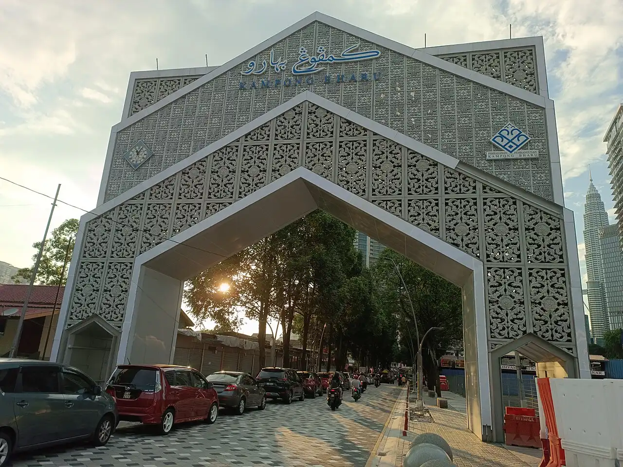 Entrance arch to Kampung Baru Kuala Lumpur with intricate patterns, cars on the street, and Petronas Twin Towers in background