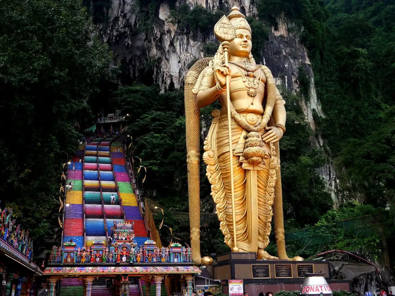 The majestic golden statue of Lord Murugan stands tall beside the vibrant, colorful stairs leading to the Batu Caves in Malaysia