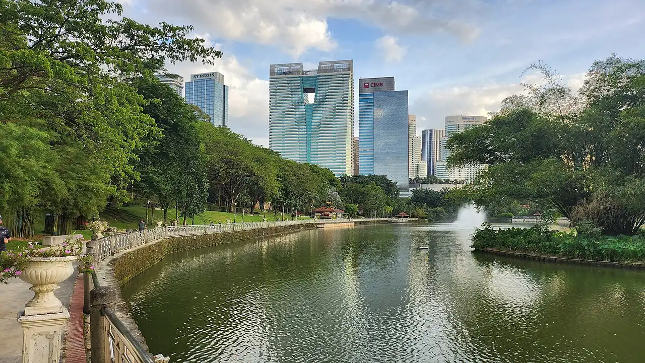 A tranquil lake in Perdana Botanical Gardens, Lake Gardens, bordered by lush trees and modern Kuala Lumpur skyscrapers