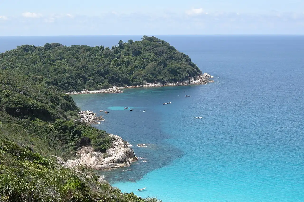 Panoramic view of the Perhentian Islands' tropical coastline with lush green hills, clear turquoise waters, and small boats