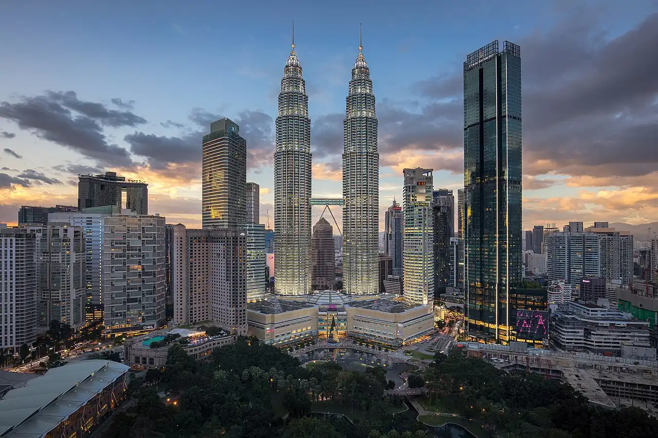 The iconic Petronas Twin Towers KLCC illuminated at twilight, standing tall amidst Kuala Lumpur's vibrant skyline and lush park