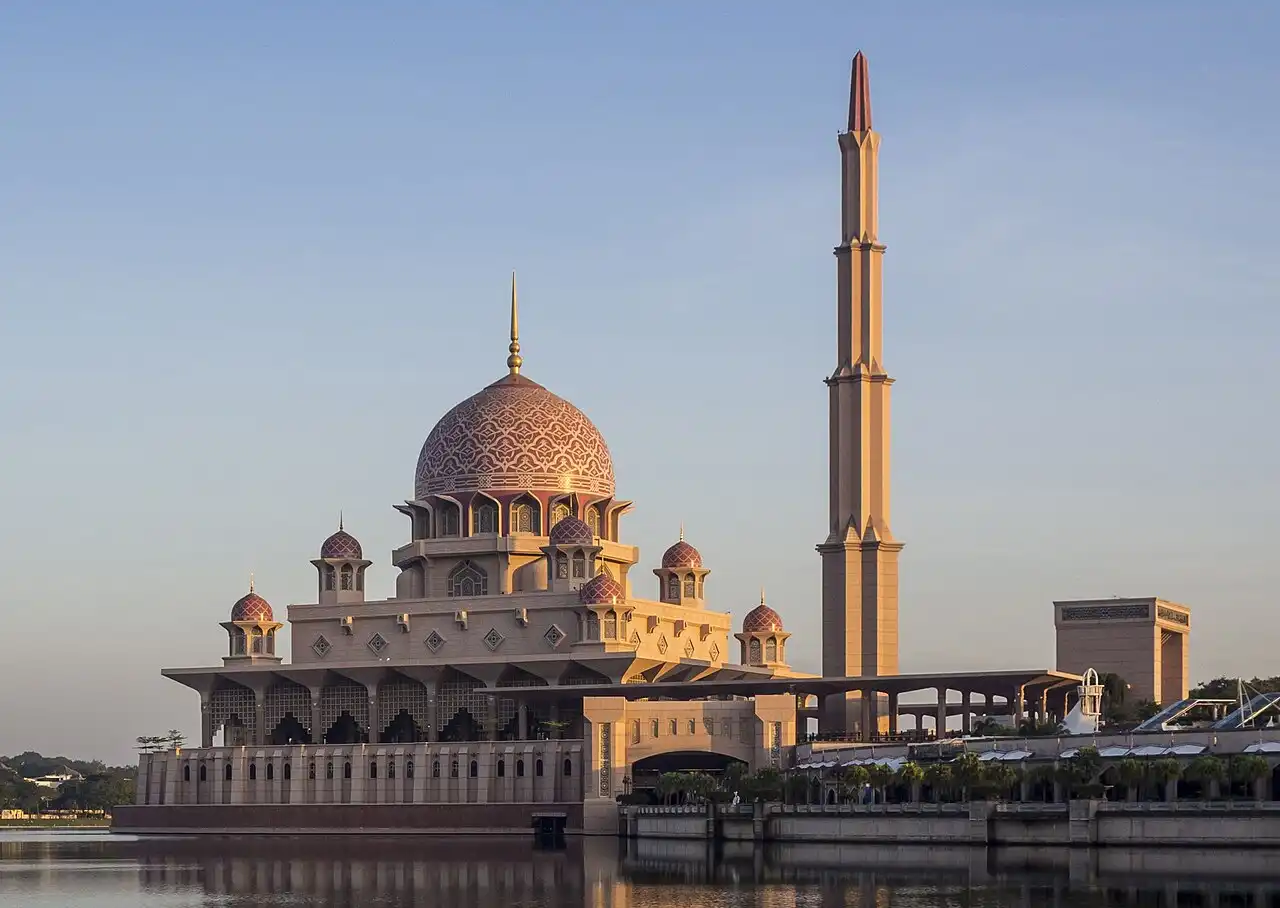 Putra Mosque in Putrajaya, Malaysia, with its iconic pink dome and tall minaret, beautifully reflected in the water.