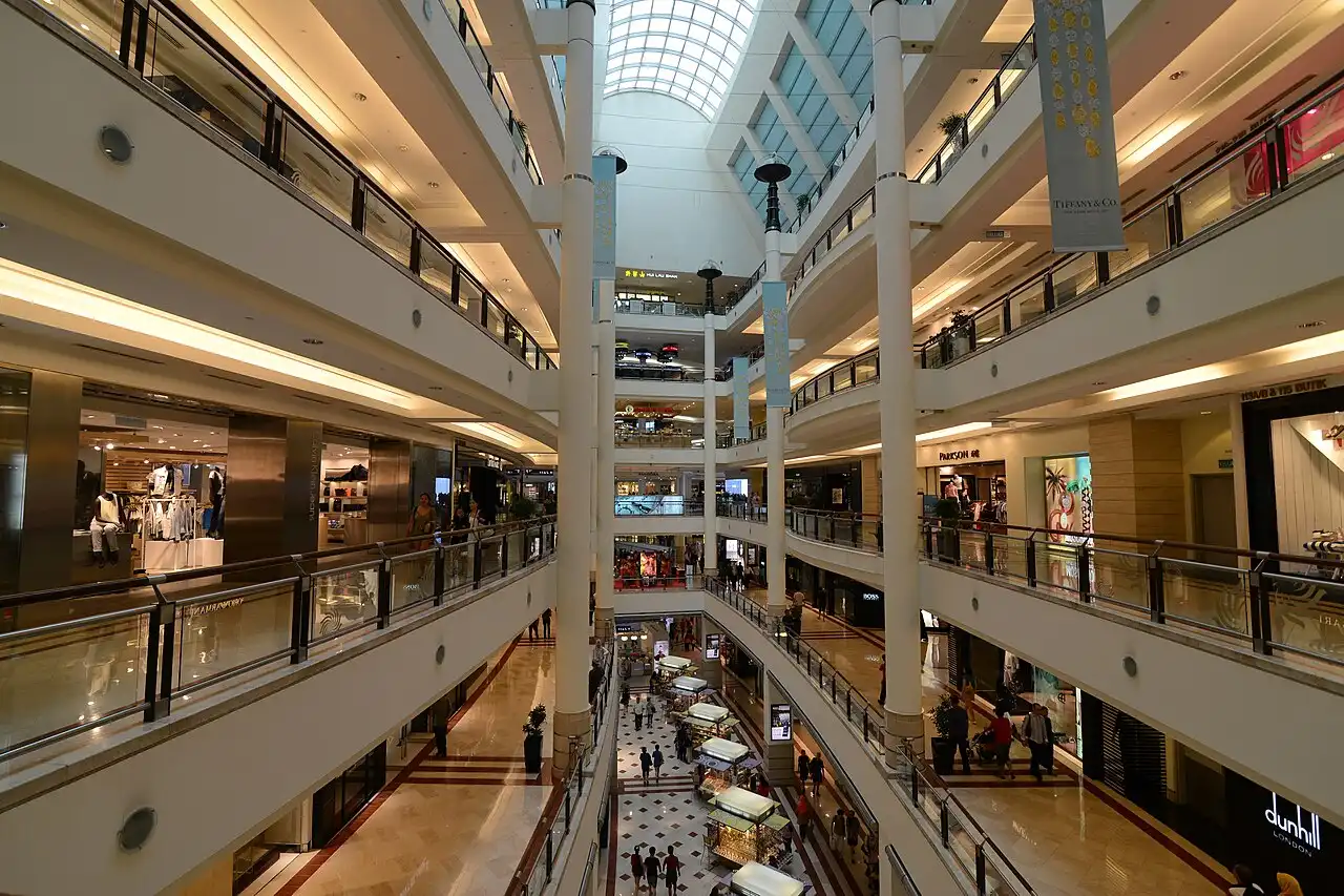Interior view of Suria KLCC, a multi-level luxury shopping mall in Kuala Lumpur with stores, escalators, and a skylight roof
